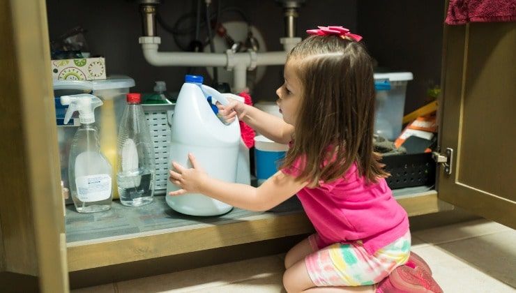 Bambino gioca con detersivi sotto il lavello